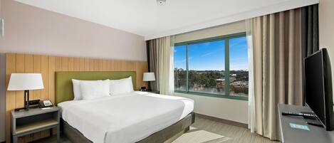 A hotel room with a bed, two bedside tables, a TV, and a window with a city view.