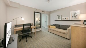 A hotel room with a desk, office chair, and a sofa with a throw pillow.