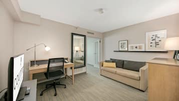 A hotel room with a desk, office chair, and a sofa with a throw pillow.