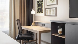 A hotel room with a desk, chair, coffee machine, and artwork on the wall.