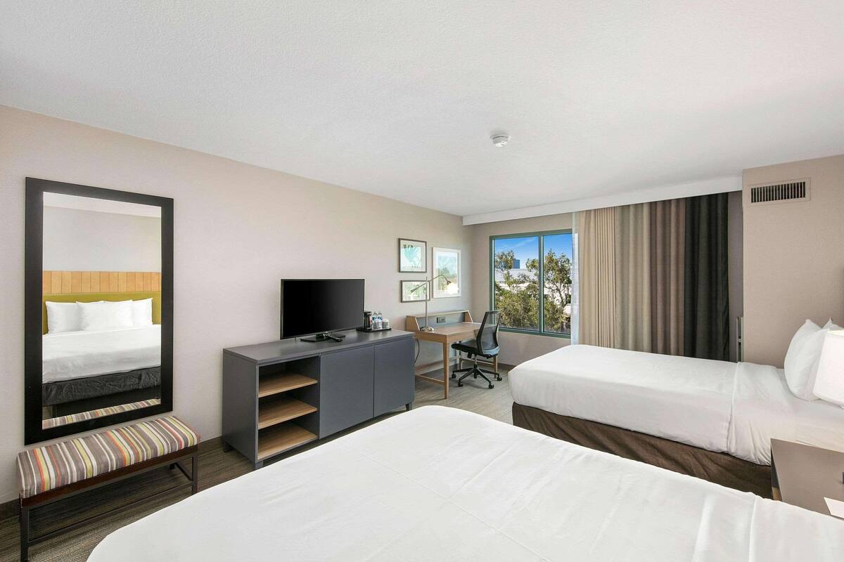 Une chambre d’hôtel avec deux lits, un bureau, une chaise, une télévision et une grande fenêtre avec des rideaux.