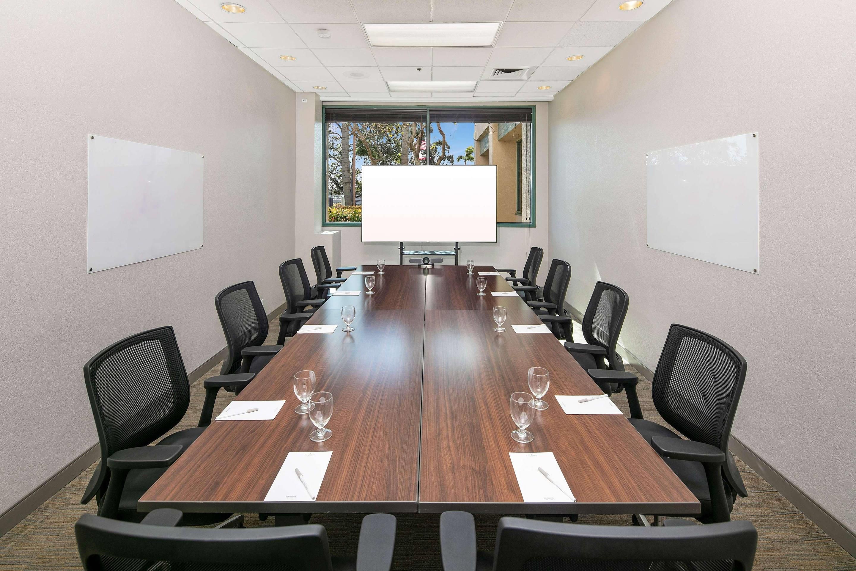 A conference room with a long table, black chairs, and two whiteboards on the walls.