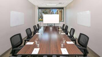 A conference room with a long table, black chairs, and two whiteboards on the walls.
