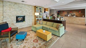 A modern living room with a stone wall, a fireplace, a sectional sofa, a coffee table, and a reception desk with a wooden backdrop. - Country Inn & Suites by Radisson, San Diego North, CA (San Diego)
