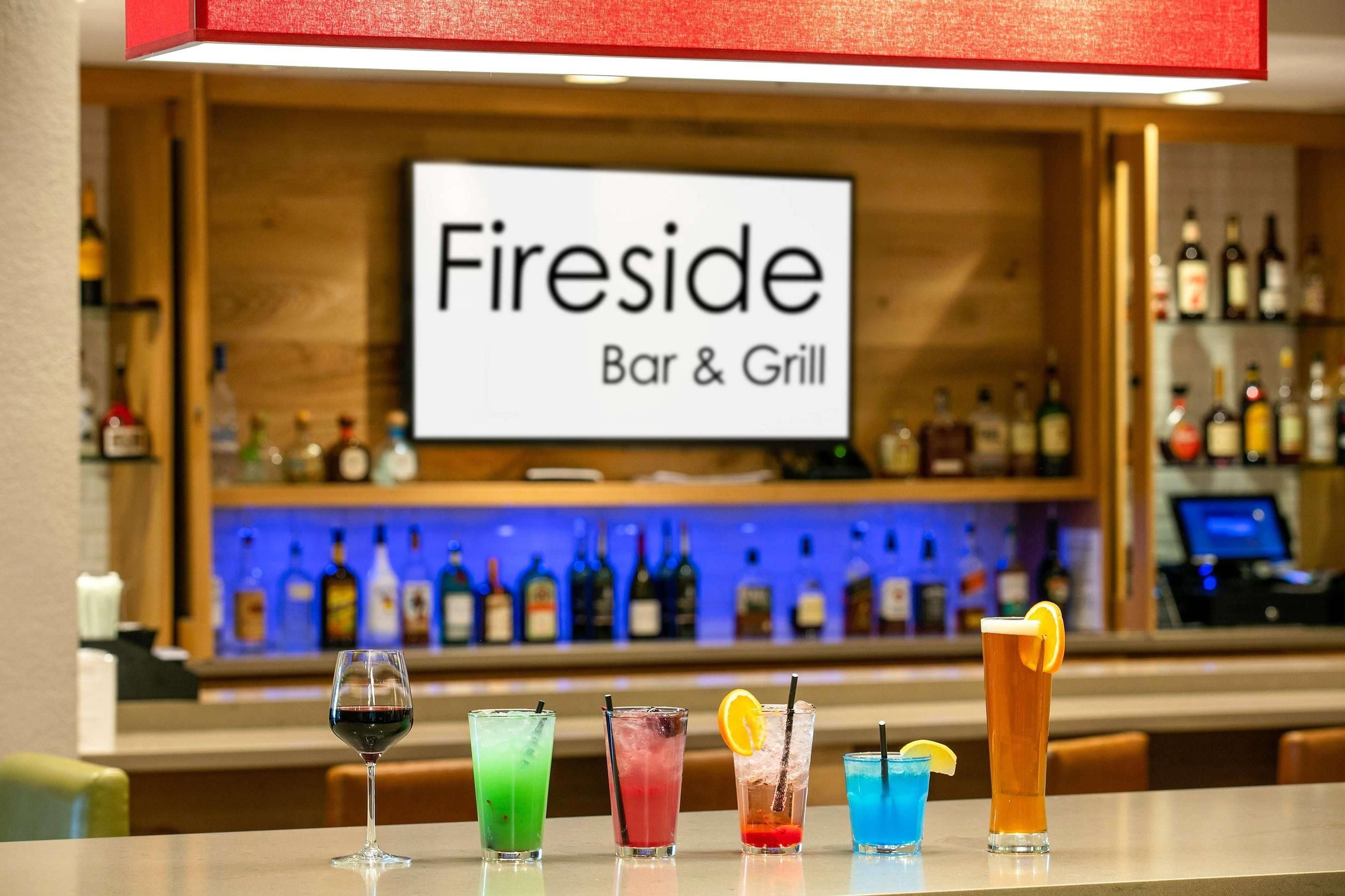 A bar area with a sign reading 'Fireside Bar & Grill' and various colorful drinks on the counter.