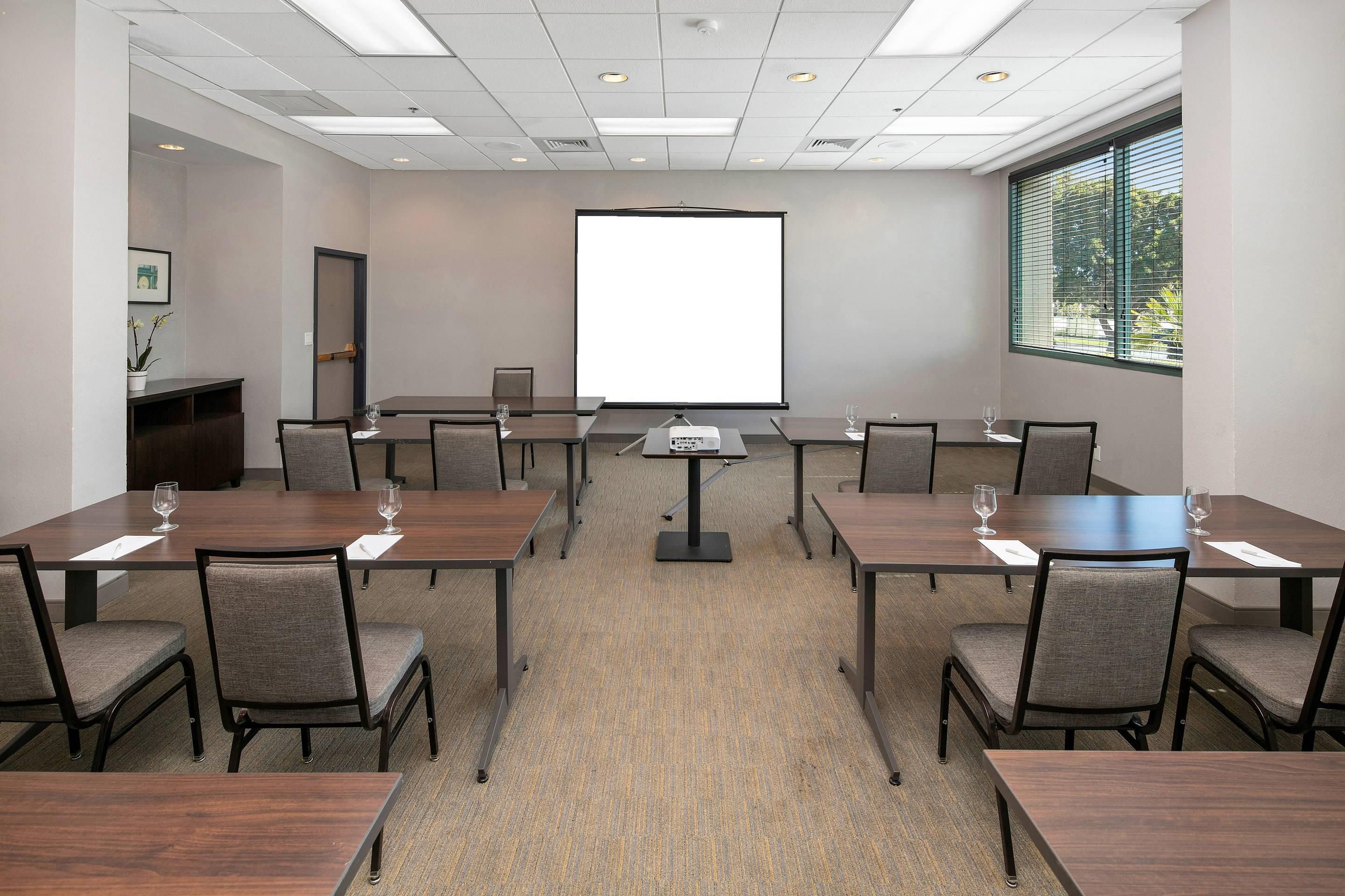 A conference room with a large projection screen, multiple tables, and chairs.