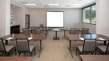 A conference room with a large projection screen, multiple tables, and chairs.
