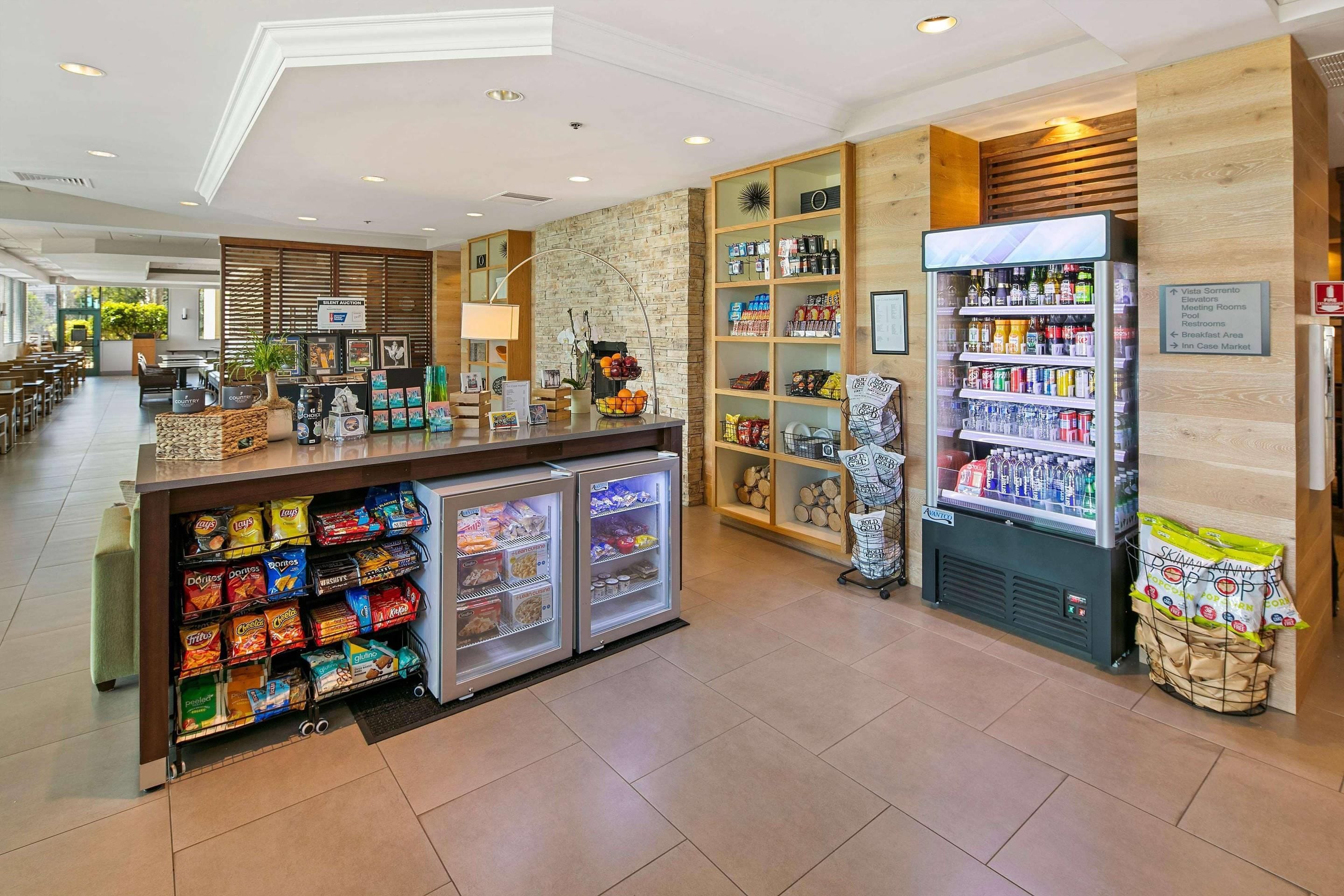 Vestíbulo de hotel con un bar de aperitivos, zona de estar y un letrero que indica servicios como ascensores, salas de reuniones y una piscina.