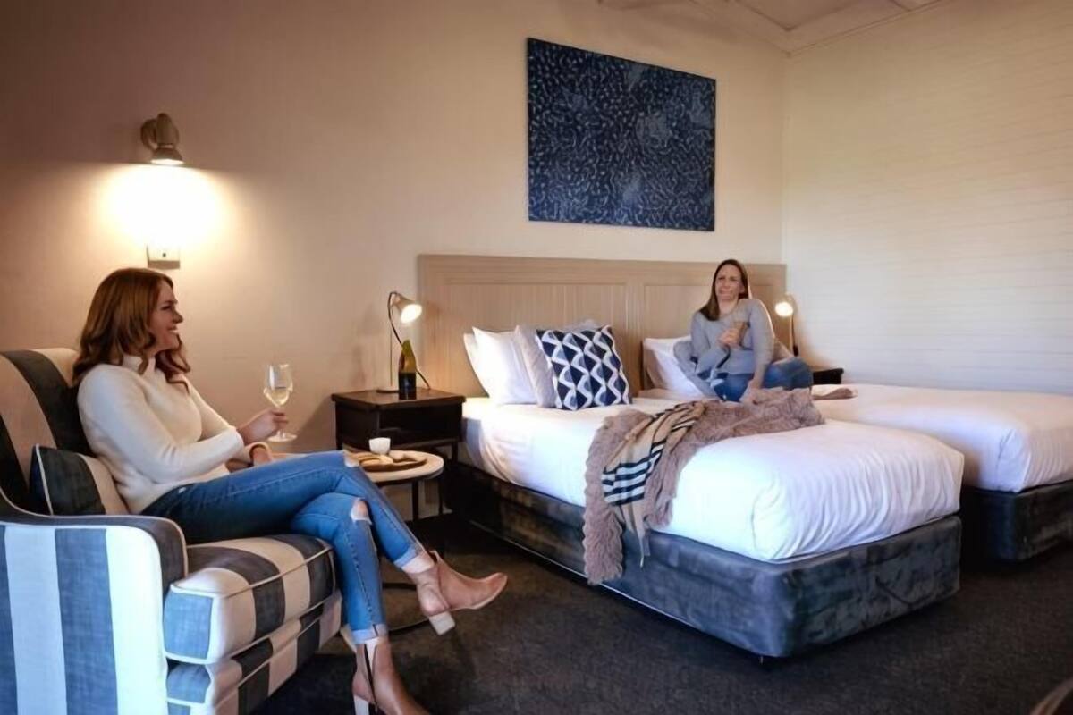 A hotel room with a bed, a sofa, a bedside table, and a wall-mounted lamp.