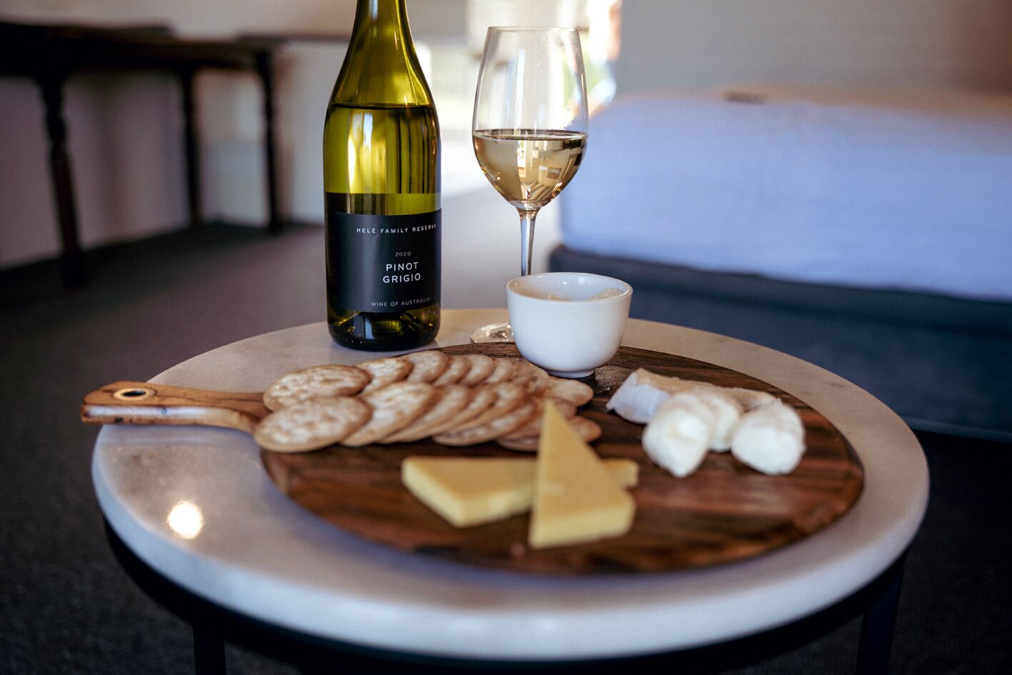 Uma mesa redonda com uma garrafa de vinho, um copo de vinho e um prato de queijo e biscoitos.