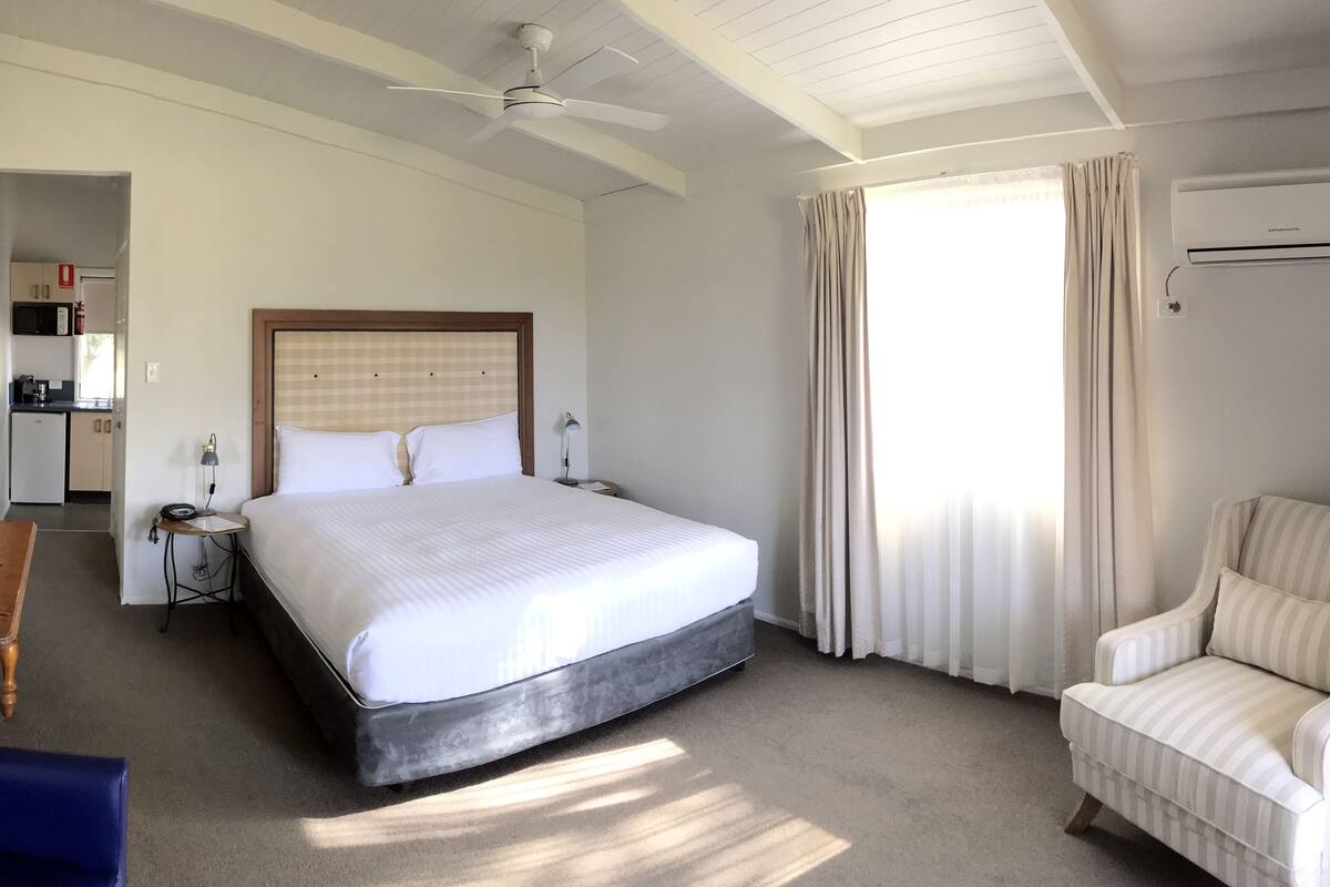 A hotel room with a large bed, a chair, a desk, and a ceiling fan.