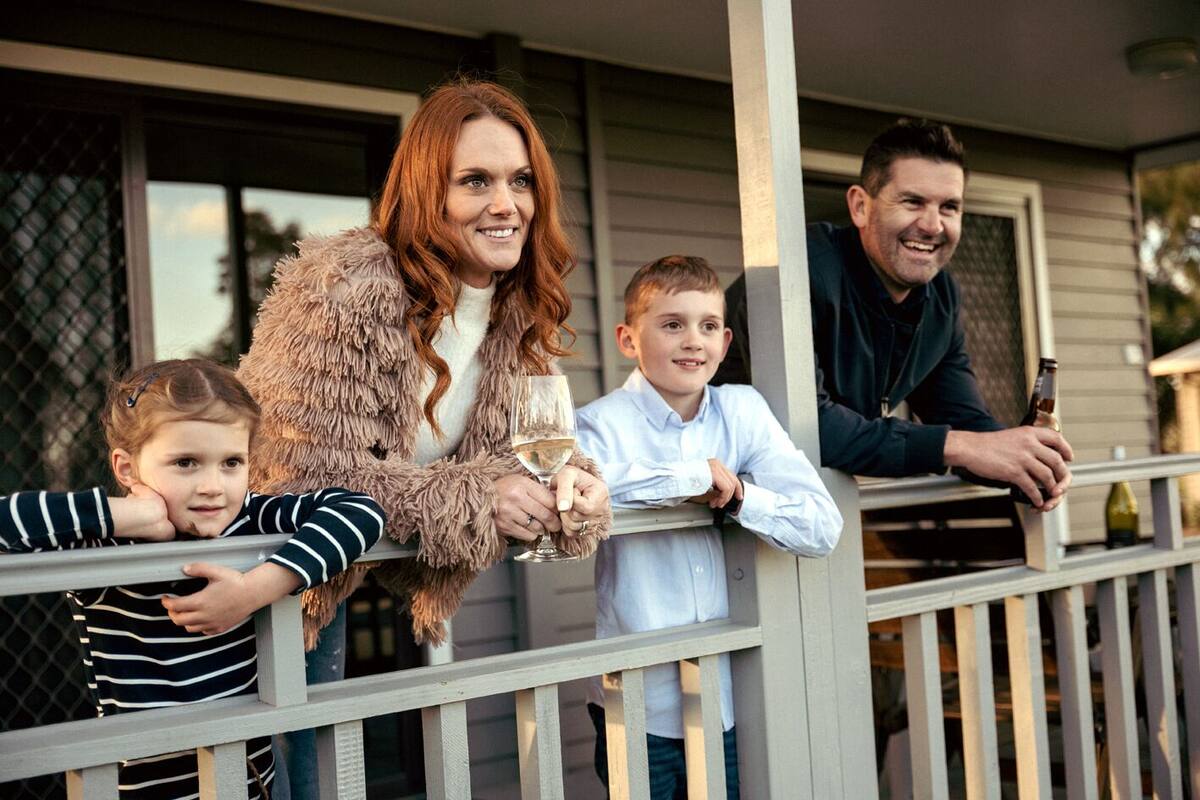 A family on a porch with a railing, a child leaning on the railing, and a bottle of beer in the background.