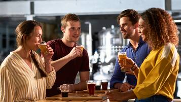 A group of people sitting around a wooden table with glasses of beer, in a setting with industrial-style background.