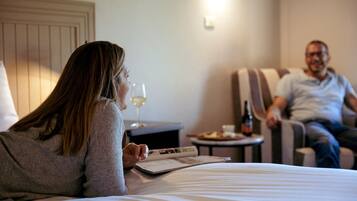Una camera d'albergo con un letto, un comodino con un bicchiere di vino, un piatto di cibo e una bottiglia di birra.