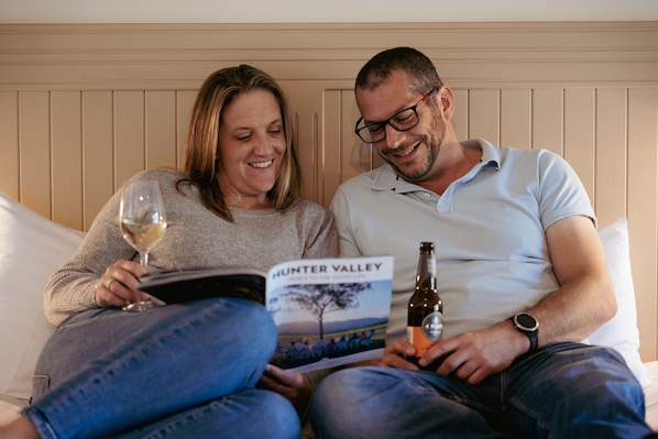 A couple sitting on a bed with a book titled "Hunter Valley" and a bottle of wine. - Hunter Valley Resort (Pokolbin)