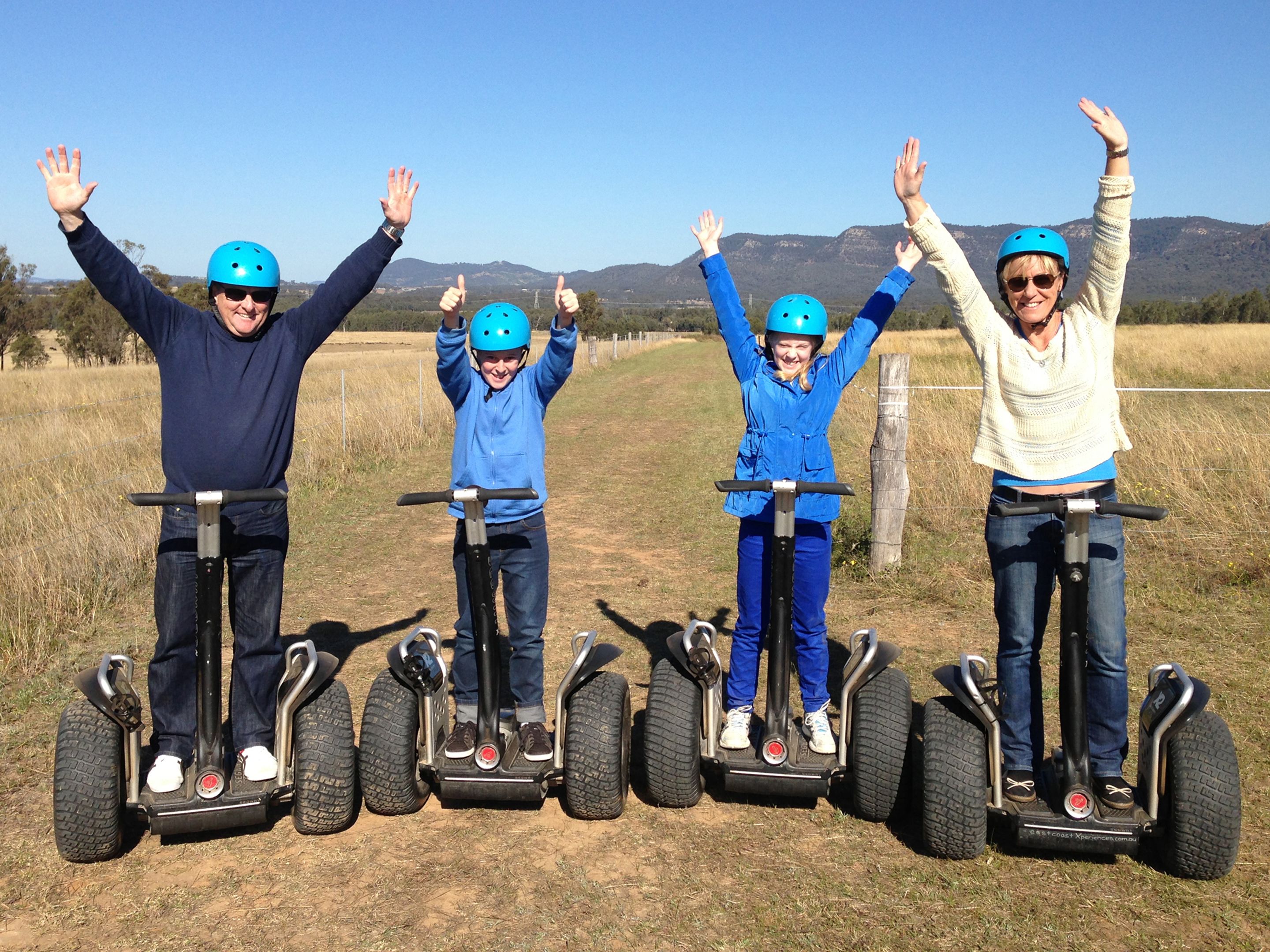 Four people on segways in a field with mountains in the background.