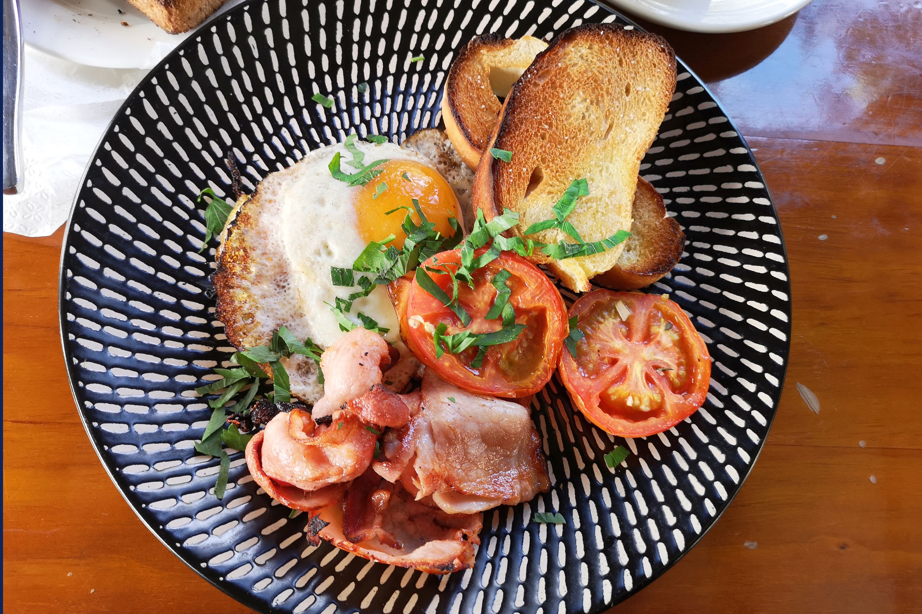 A plate with a fried egg, bacon, tomatoes, and toast.