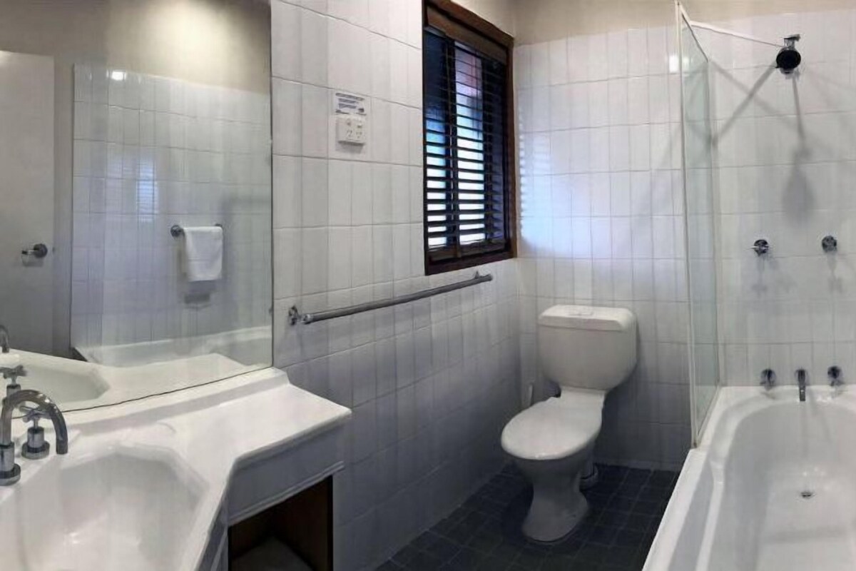 A bathroom with a white sink, toilet, and bathtub. There is a window with blinds, a towel rack, and a shower area.