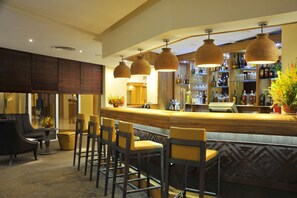 Uma área de bar com balcão de madeira, vários banquetas e luminárias pendentes.