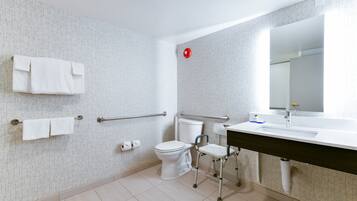A modern bathroom with a toilet, bidet, handrails, a sink, and a mirror.