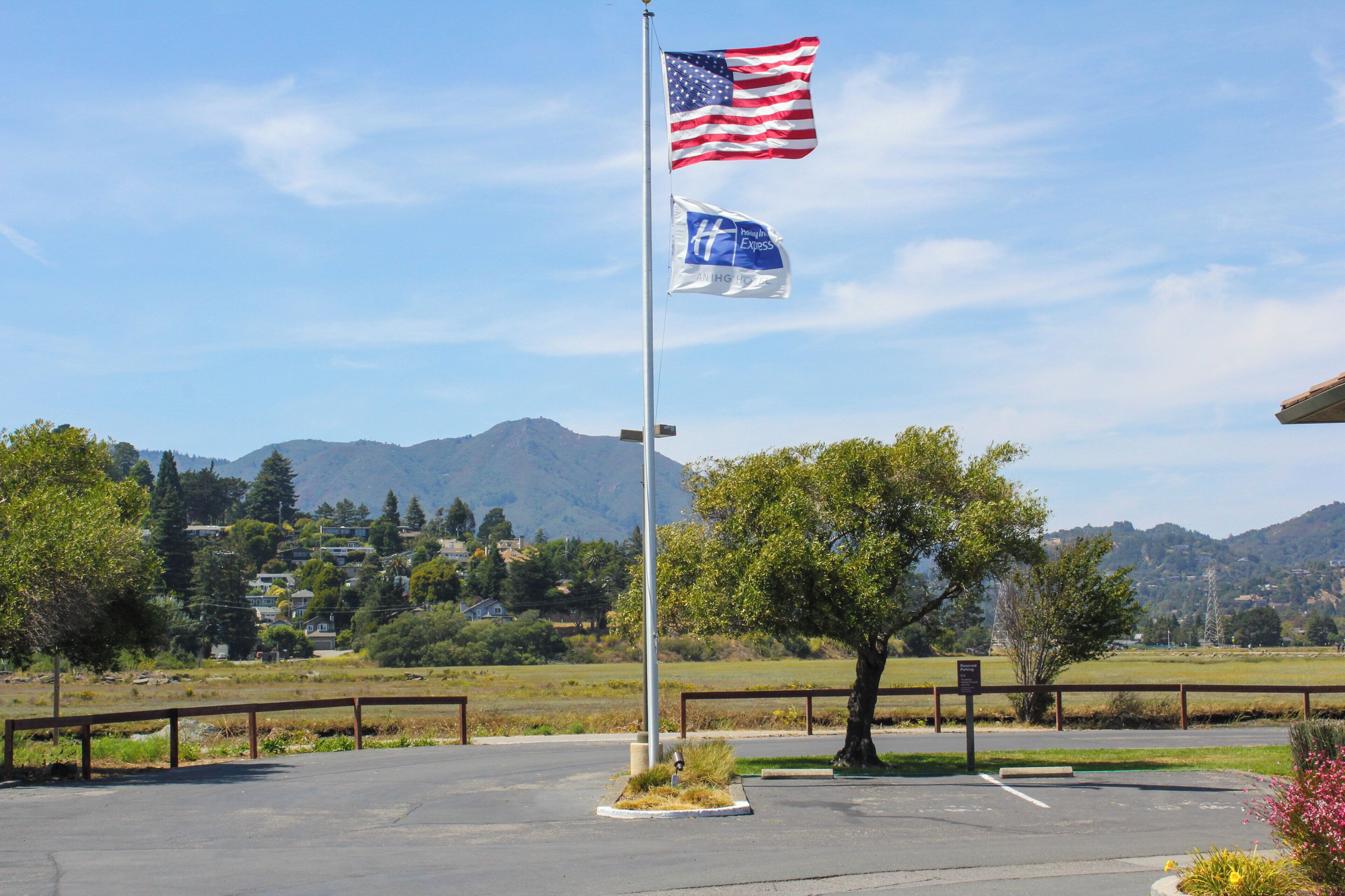 Un mât sur lequel flottent le drapeau américain et le drapeau de l’hôtel, entouré d’un parking avec une chaîne de montagnes en arrière-plan.