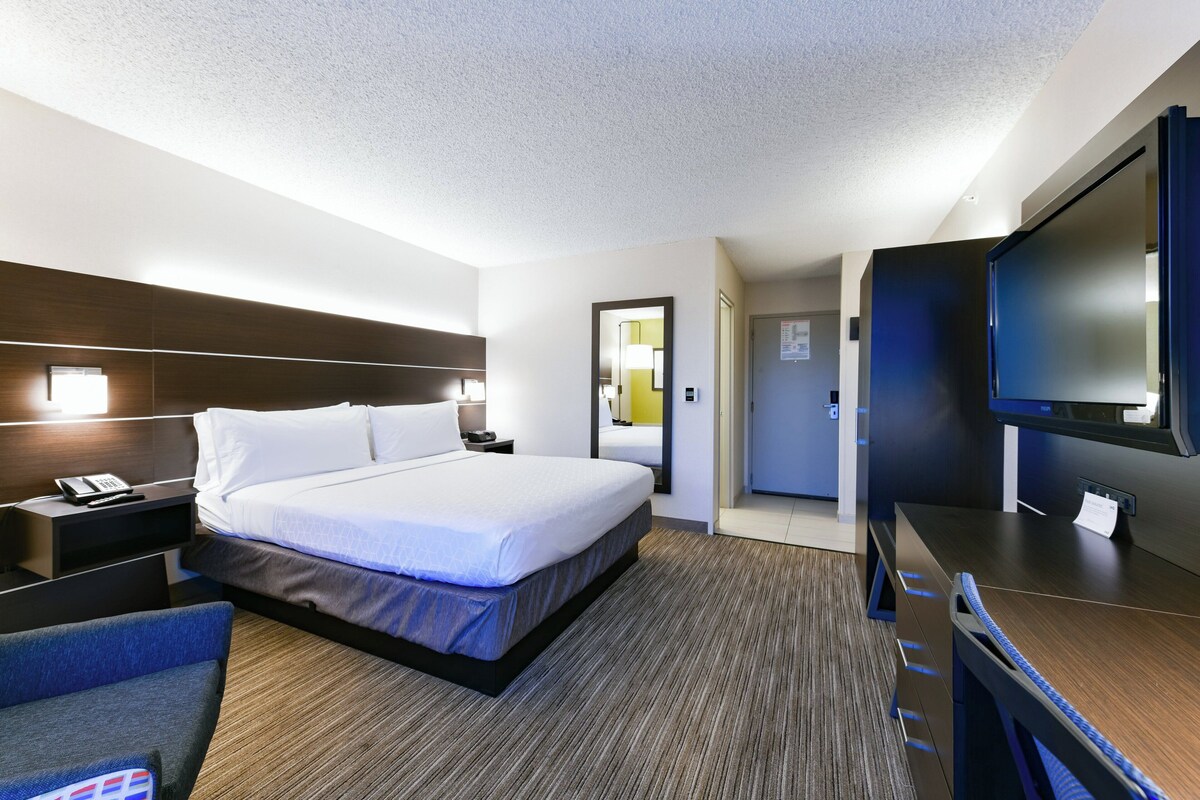 A hotel room with a large bed, a desk with a flat-screen TV, a chair, and a nightstand with a phone.