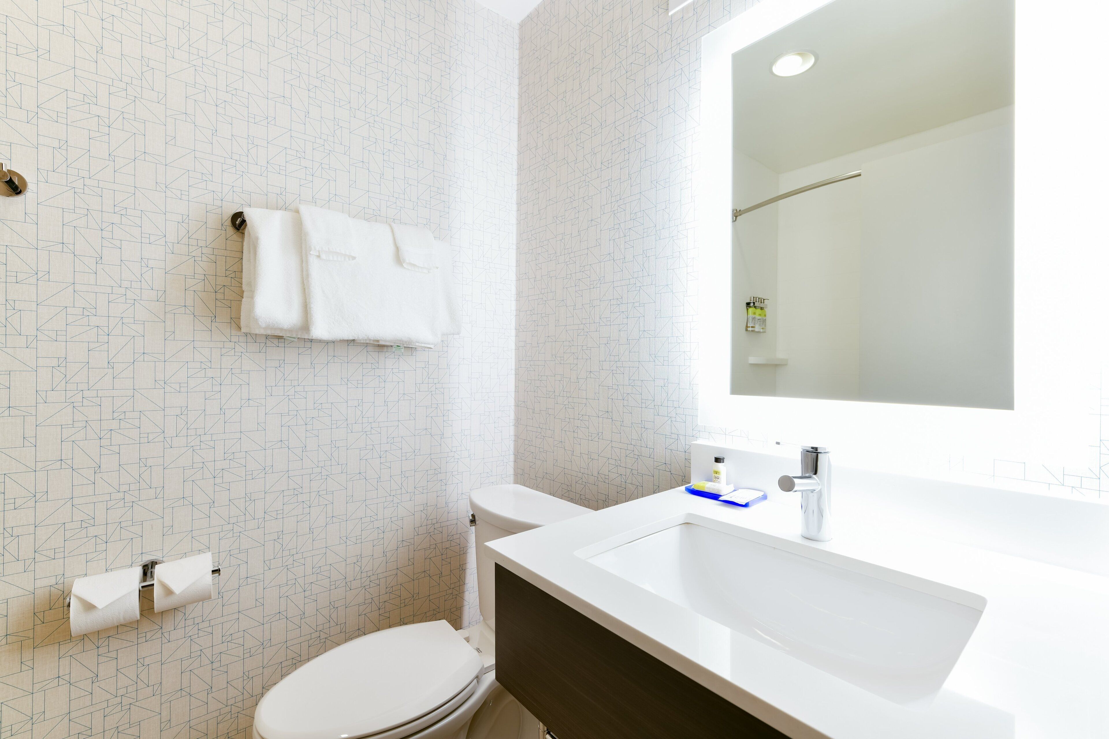 Un bagno moderno con un water bianco, un asciugamano appeso al muro e uno specchio grande sopra il lavabo.