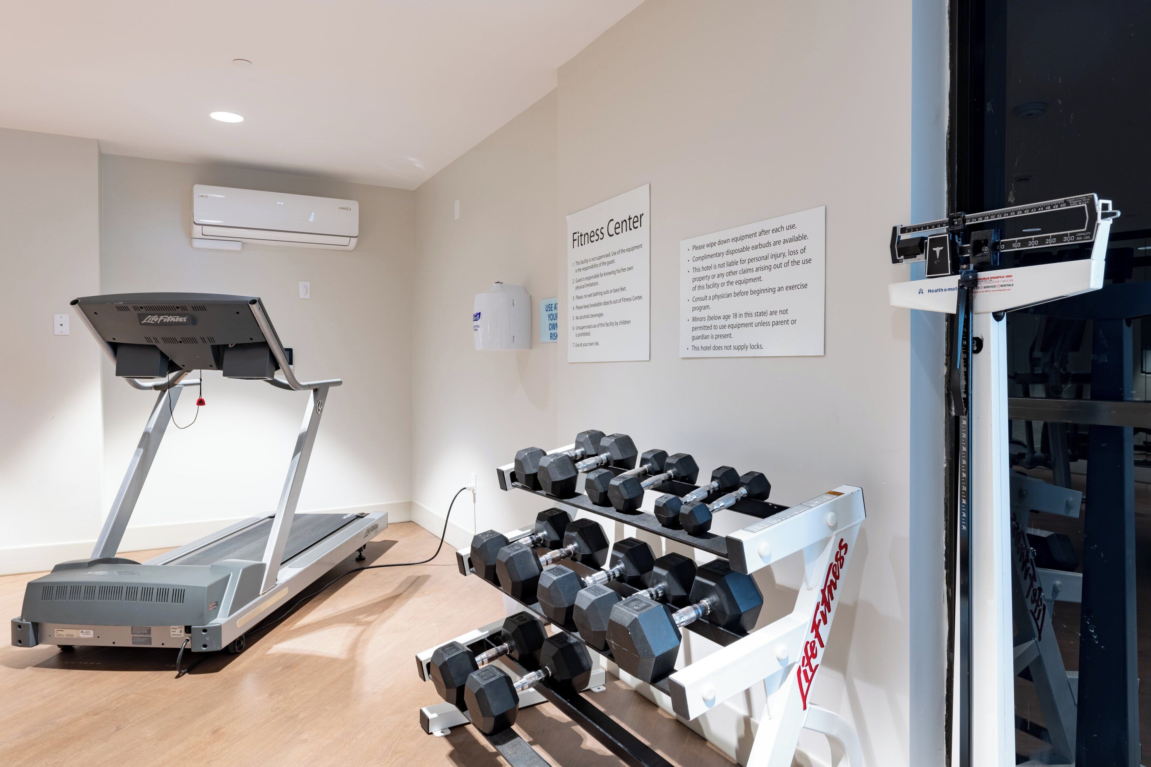 A fitness center with a treadmill, dumbbells, and a weight scale.