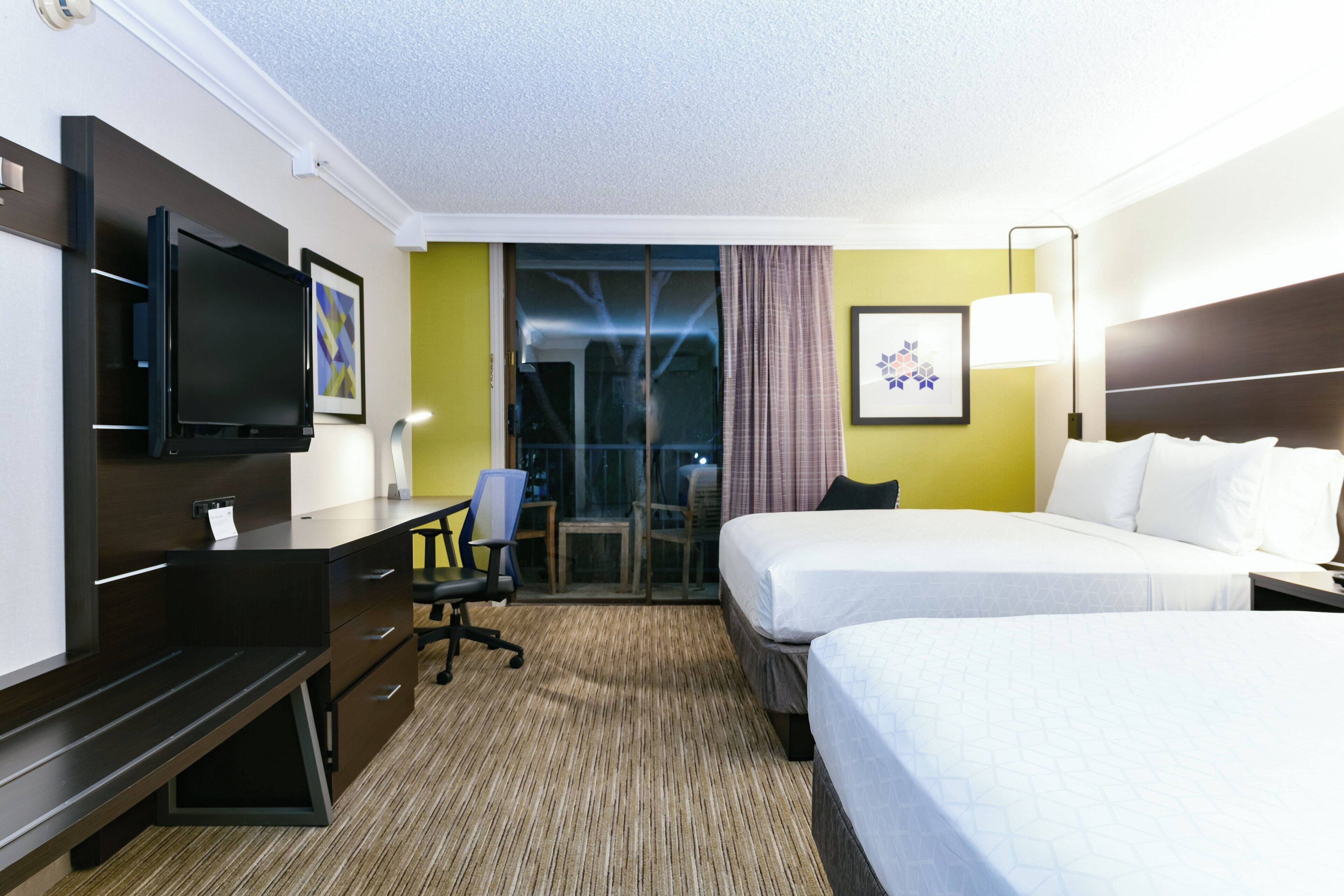 Ein Hotelzimmer mit einem Bett, einem Schreibtisch, einem Stuhl, einem Fernseher und einem fenster mit Vorhängen.