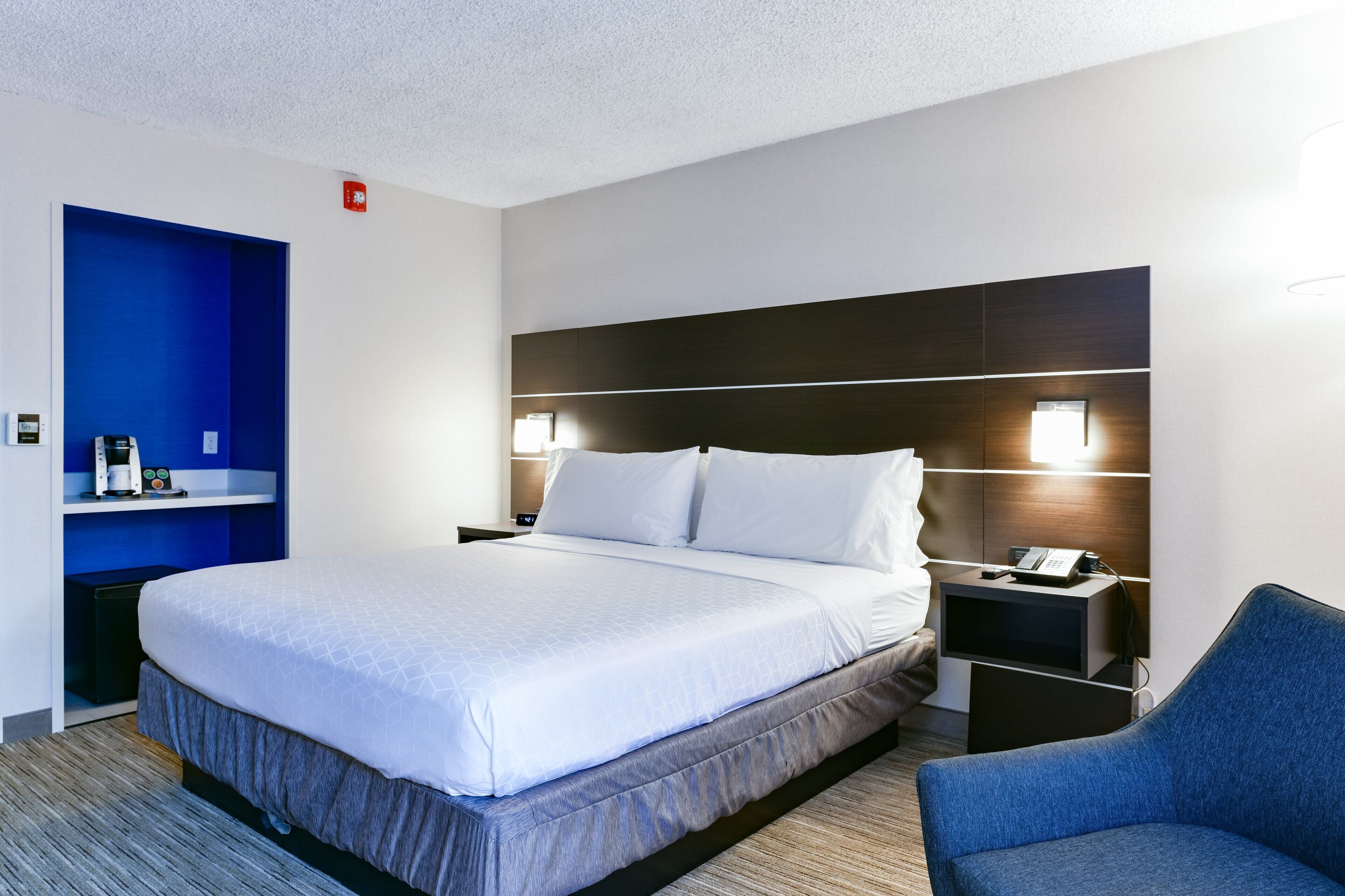 A hotel room with a large bed, bedside tables, a chair, and a blue accent wall.