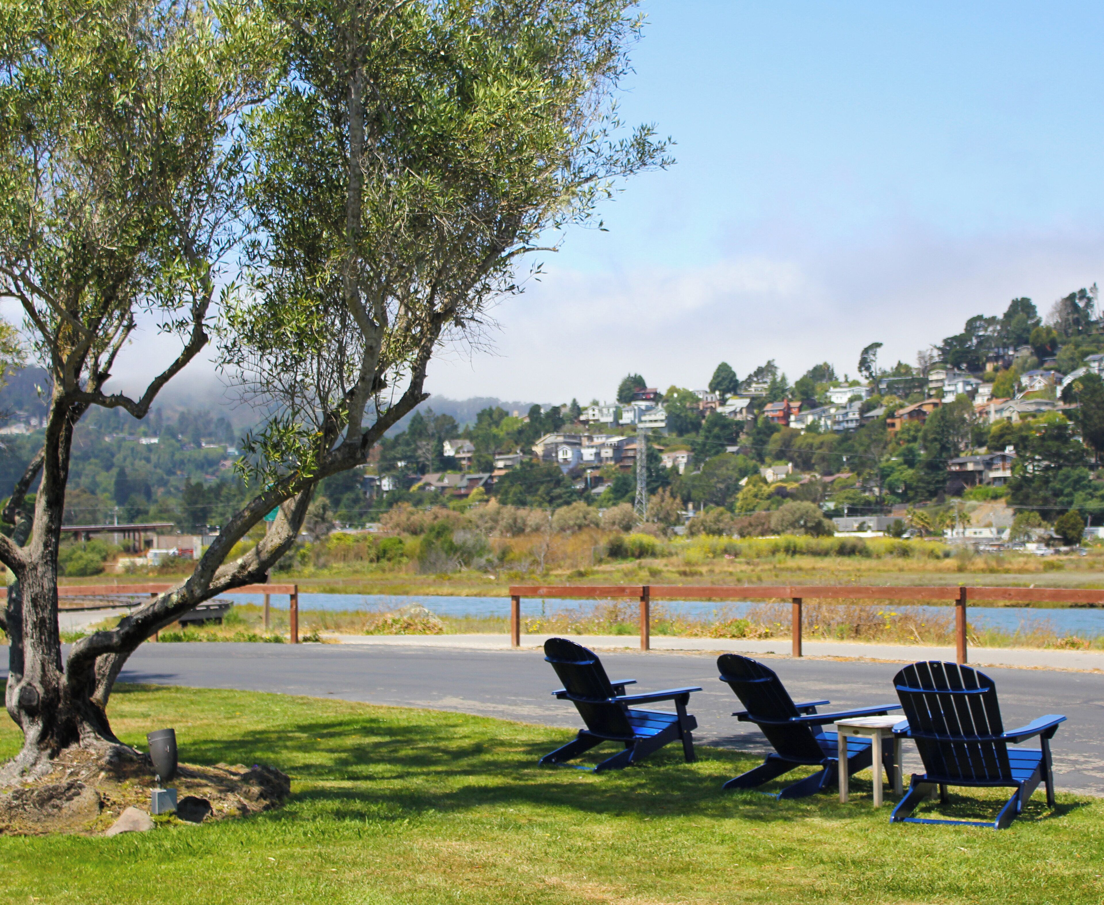 Un parque con dos sillas Adirondack y una mesa de picnic, con vista a una zona residencial con casas y una masa de agua.