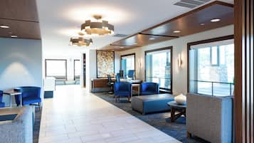 A modern hotel lobby with a reception desk, seating area, and large windows.