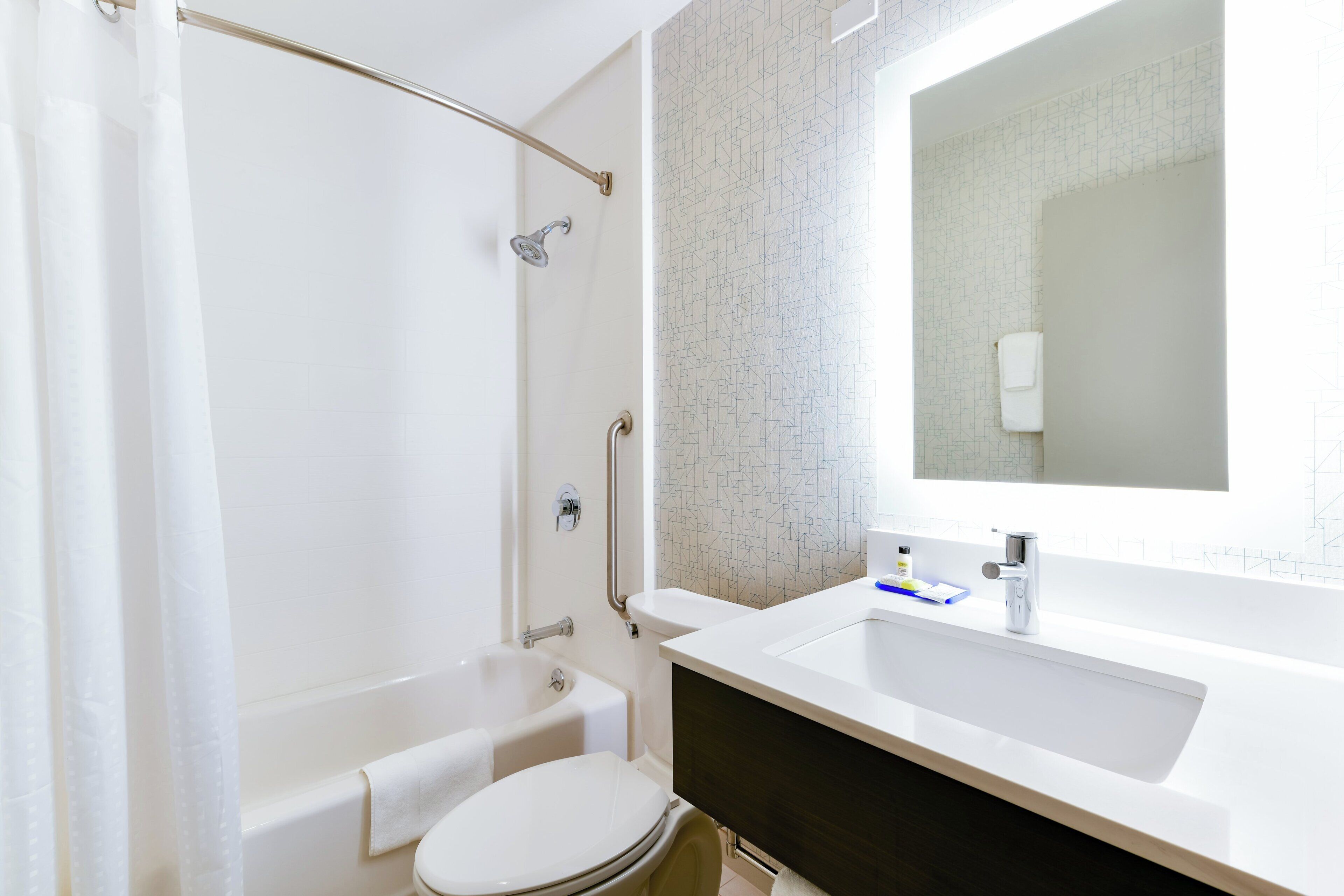 Un baño con bañera, inodoro y lavamanos con un espejo arriba.