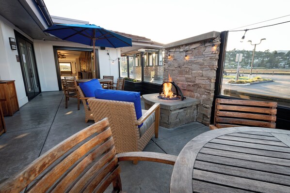 An outdoor patio with a stone wall, a fire pit, wooden furniture, and a blue umbrella. - Holiday Inn Express Mill Valley San Francisco Area by IHG (Mill Valley)