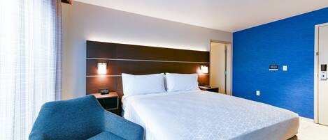 Een hotelkamer met een groot bed, een blauwe fauteuil, een nachtkastje en een aan de muur bevestigde televisie.