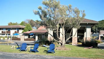A hotel with a covered patio, outdoor seating, and a large tree in the foreground.