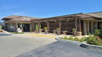 A hotel entrance with a covered outdoor area, a parking lot, and landscaped gardens.