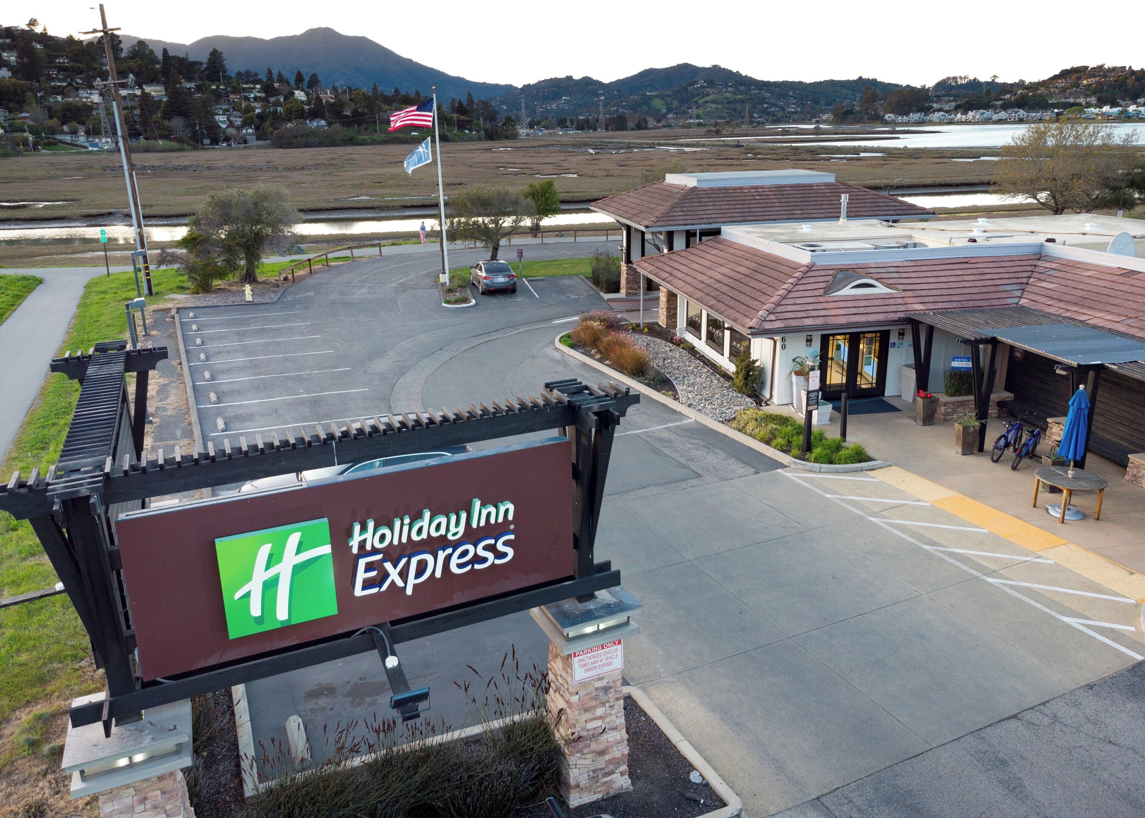 Un Holiday Inn Express con estacionamiento, un edificio de techo rojo y vistas a montañas al fondo.