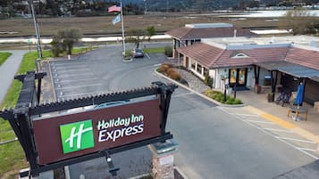 Un Holiday Inn Express con estacionamiento, un edificio de techo rojo y vistas a montañas al fondo.