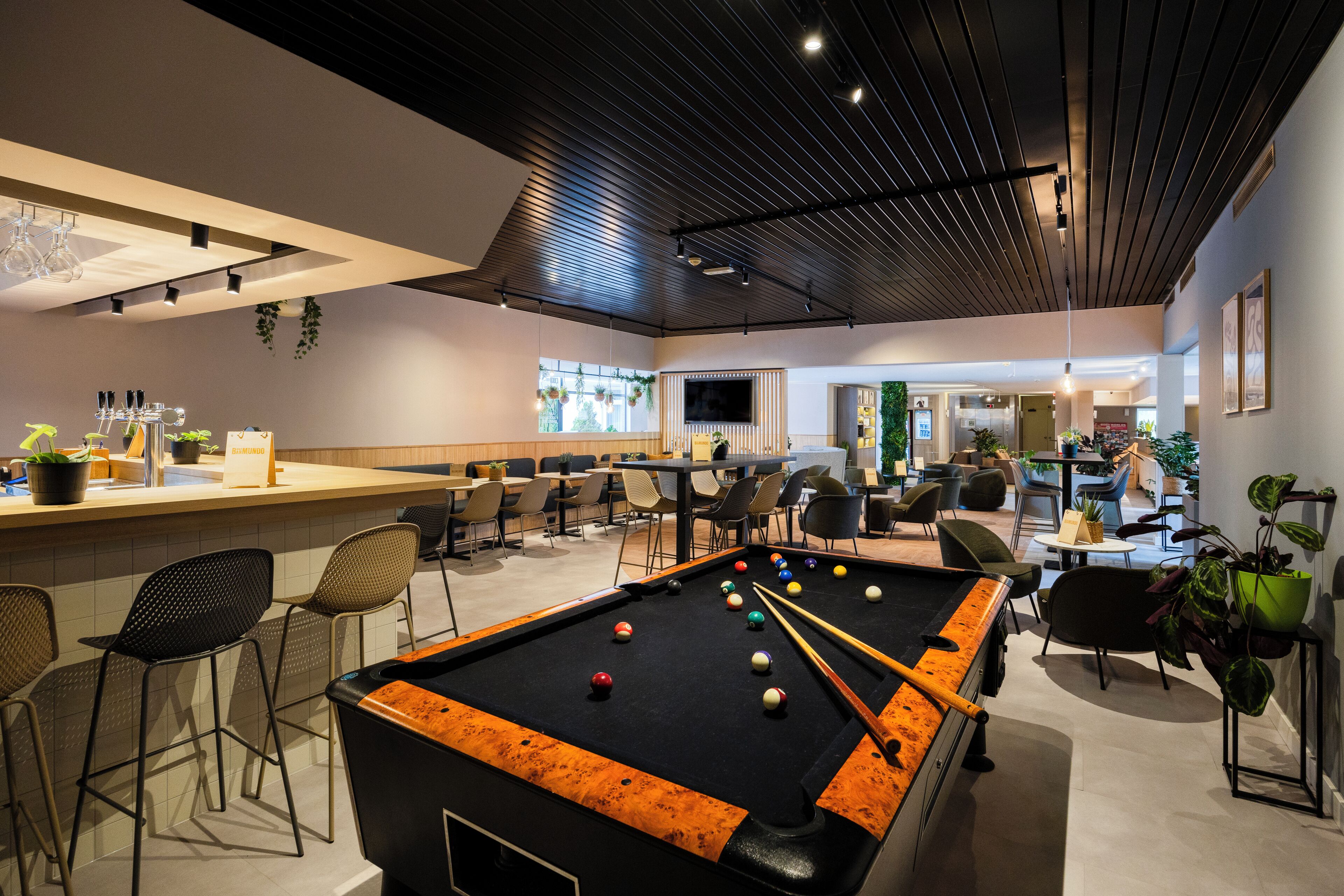 Ein Billardtisch in einer modernen Lounge mit Barhocker und Sitzgelegenheiten.