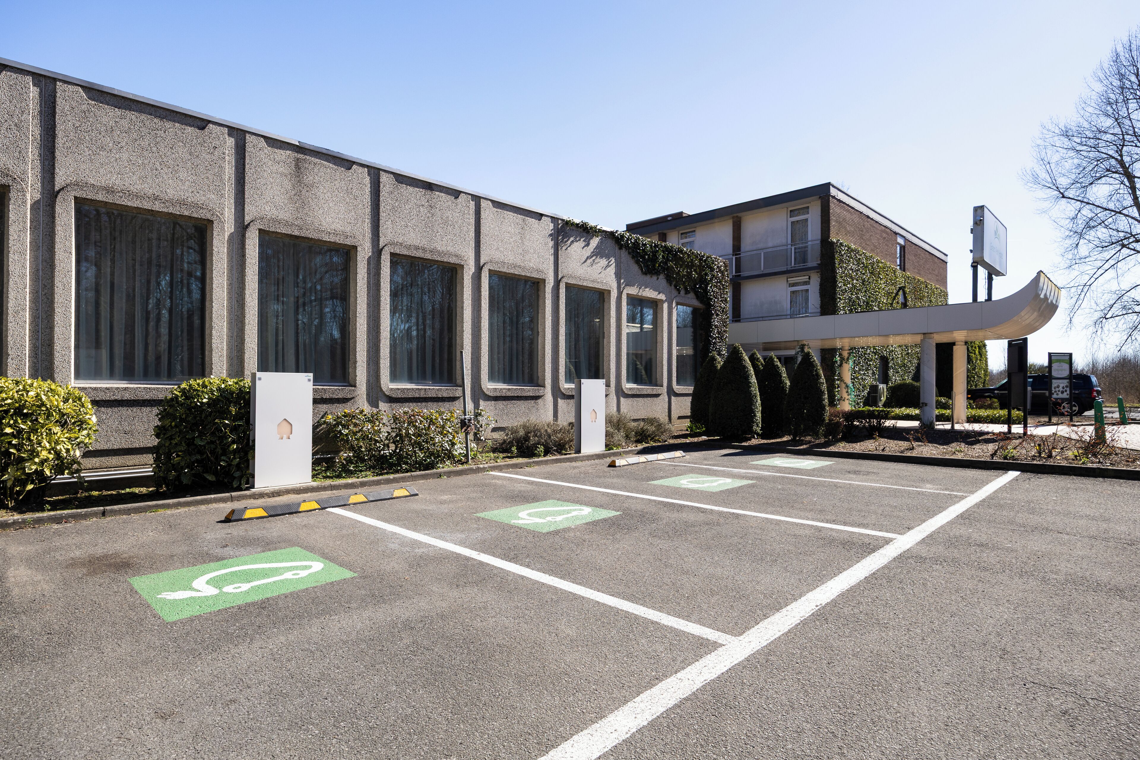 Un parking doté d’emplacements réservés aux vélos et un bâtiment avec de grandes fenêtres et une allée couverte.