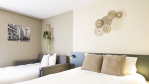 Une chambre d’hôtel avec deux lits, une œuvre d’art accrochée au mur, une plante suspendue et un élément décoratif mural.
