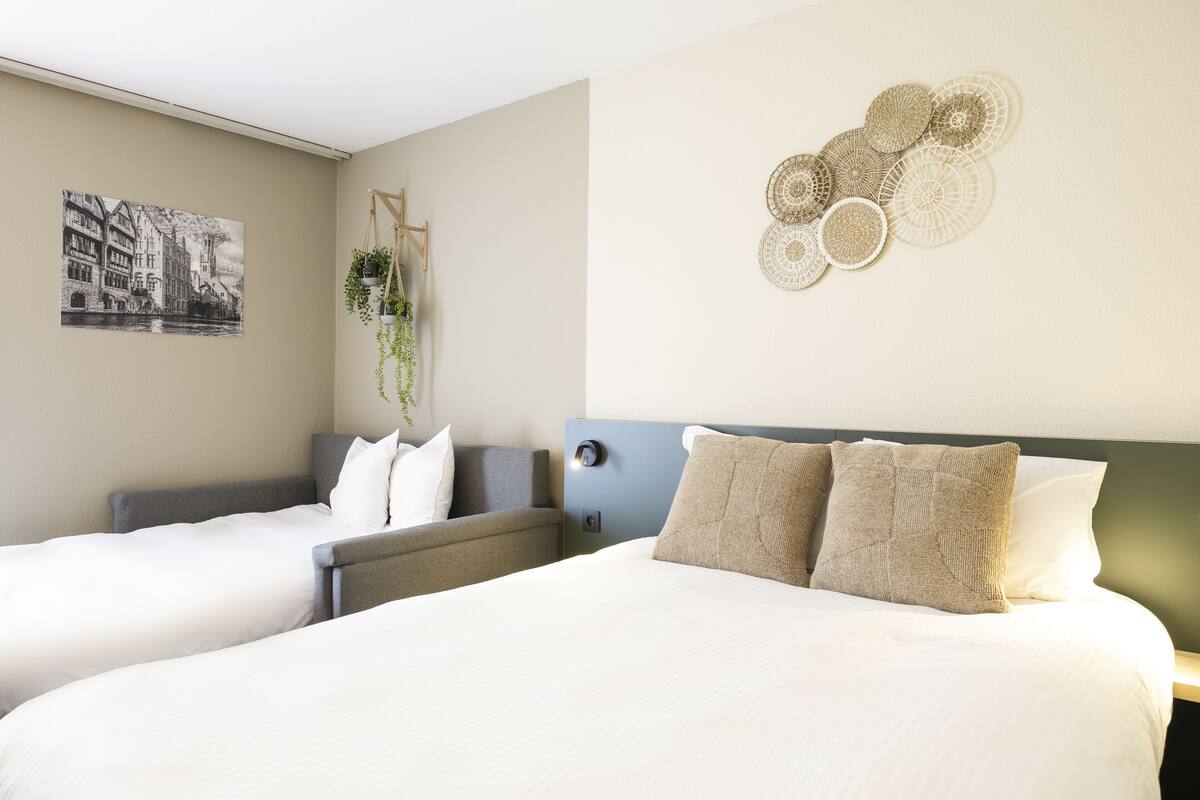 Habitació d'hotel amb dos llits, una obra penjada a la paret, una planta suspesa i una peça decorativa a la paret.