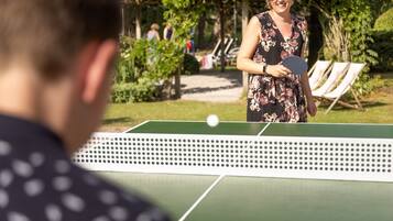 A tennis court with a net, surrounded by greenery and outdoor seating.