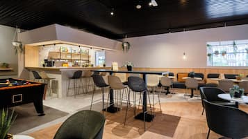 Een moderne barruimte met een pooltafel, barstoelen en een zithoek met banken en fauteuils.
