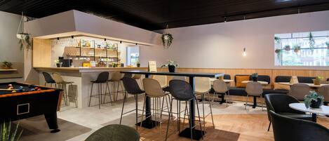 Un área de bar moderna con mesa de billar, taburetes y una zona de estar con sofás y sillones.