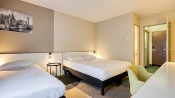 Une chambre d’hôtel avec deux lits, un bureau et une chaise. Il y a un tableau au mur et une porte qui donne sur une autre pièce.