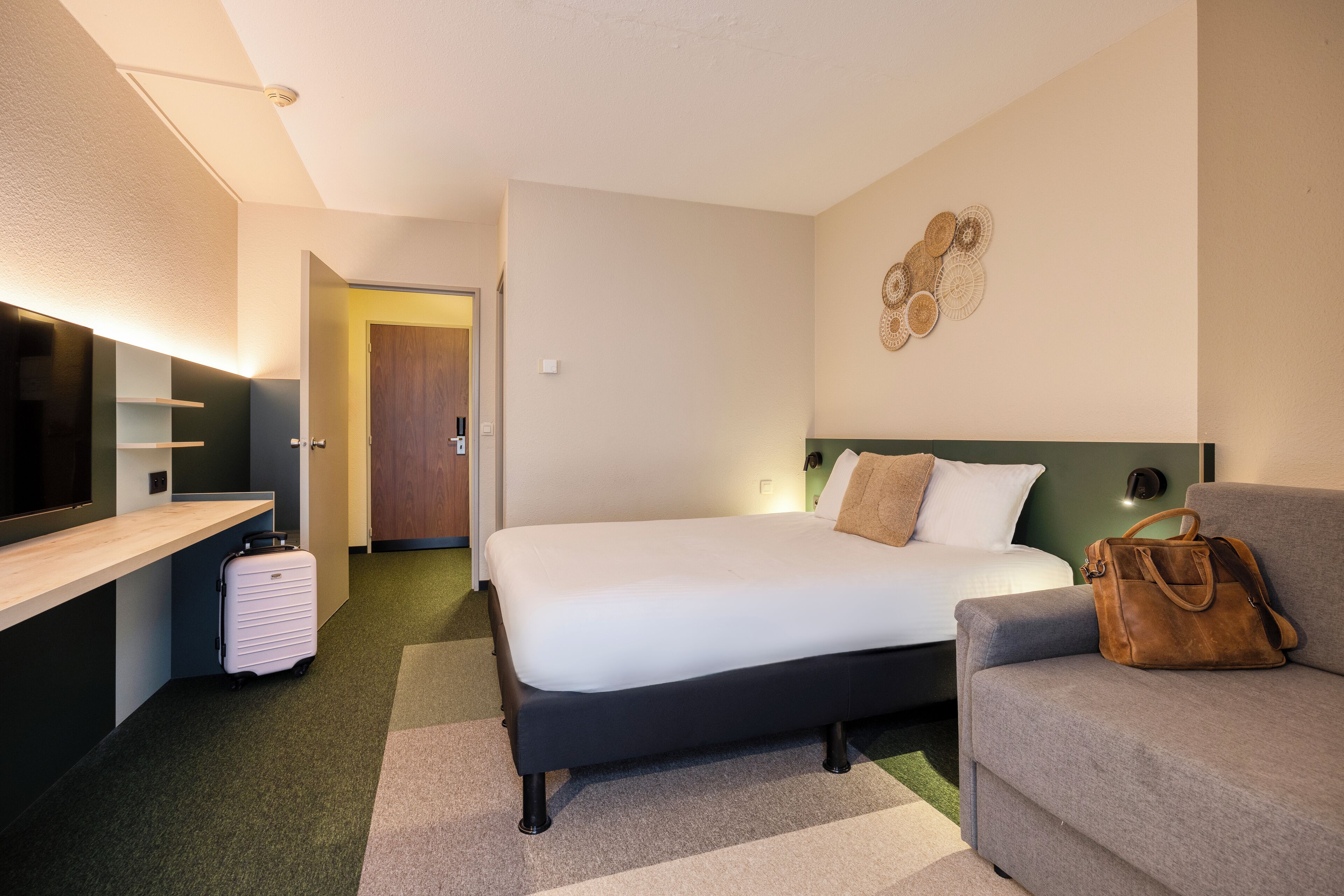 Una habitación de hotel moderna con una cama, un sofá, un escritorio y una maleta.