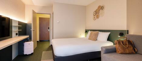 A modern hotel room with a bed, a sofa, a desk, and a suitcase.