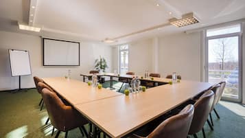 Un salón de conferencias con una larga mesa, sillas, una pantalla de proyector y una planta.